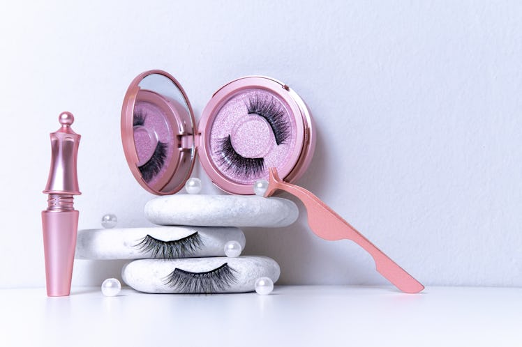 Magnetic fake artificial eyelashes in pink mirror kit, eye liner, tweezers on white background. Home...