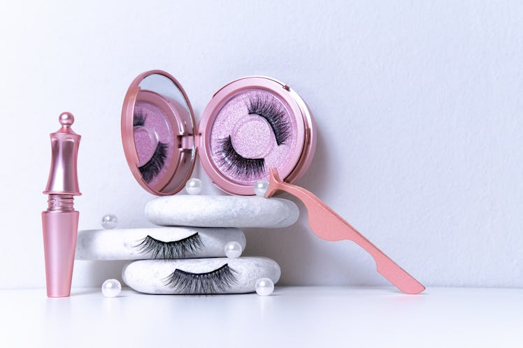Magnetic fake artificial eyelashes in pink mirror kit, eye liner, tweezers on white background. Home...