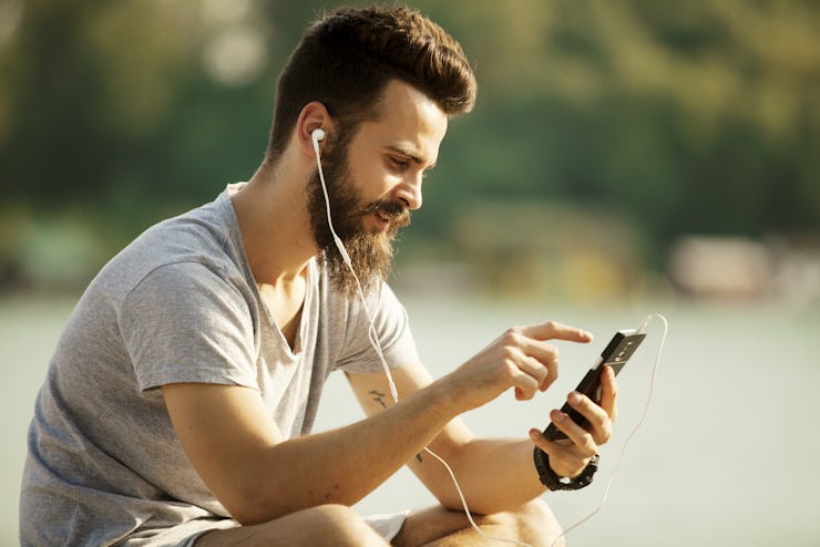 Portrait of a man with beard listening music on mobile phone outdoors