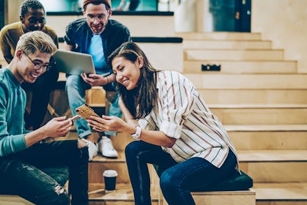 Cheerful millenial woman showing latest feed from social networks to group of multiracial friends, h...