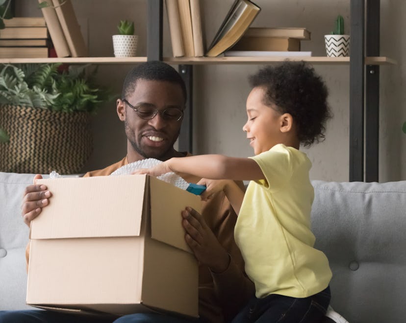 Family african father and little son opens unpack carton box sitting on sofa at home, best subscript...