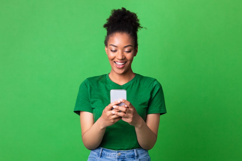 Amazing Application. Portrait of happy black woman using smartphone on green studio wall
