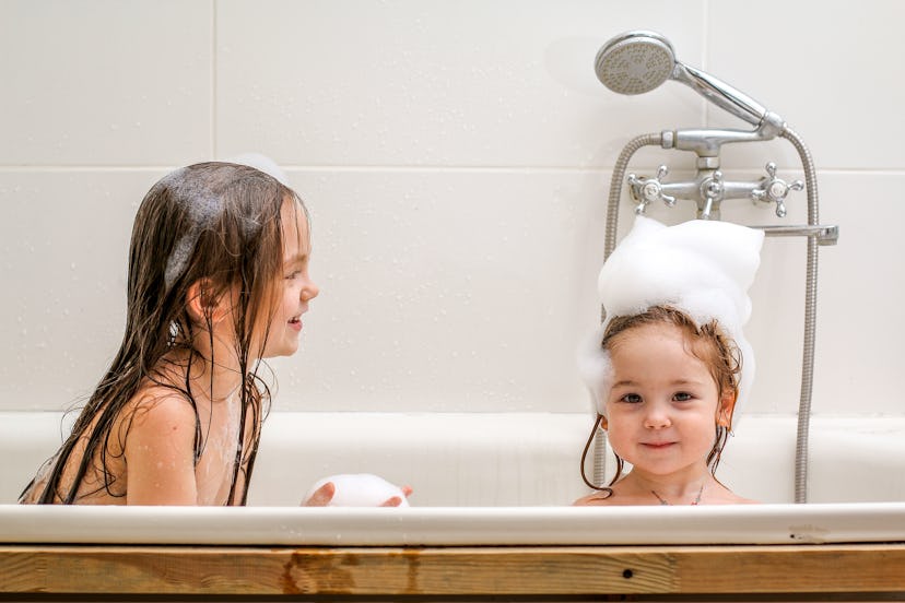 Two little sisters play in a bath with foam. 
