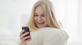 Smiling woman texting on her mobile phone lying in bed during the day.