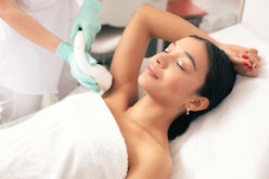 Calm young woman lying with closed eyes and putting on arm up while having laser hair removal proced...