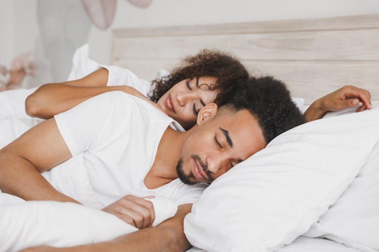 Young calm african loving couple girl guy in t-shirts lying on bed with white sheet pillow blanket i...