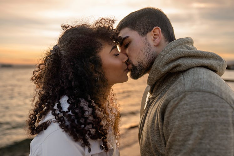 Head and shoulders portrait of young beautiful couple in love kissing at sunset in winter seaside re...