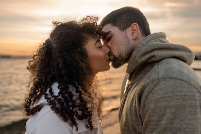 Head and shoulders portrait of young beautiful couple in love kissing at sunset in winter seaside re...