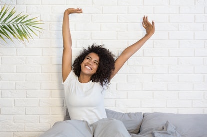 Beautiful african-american woman waking up in her bed, smiling and stretching, copy space