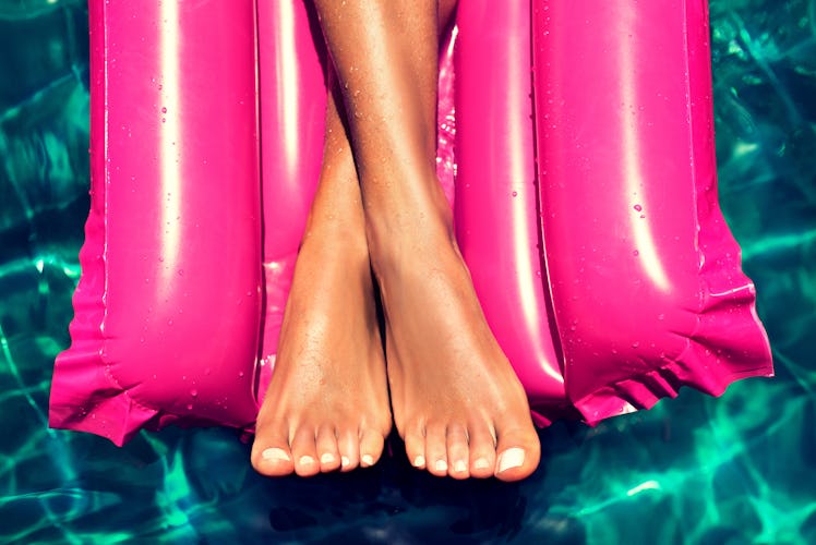 Tanned well-groomed feet in the pool on magenta inflatable mattress for swimming . Pedicure and foo...
