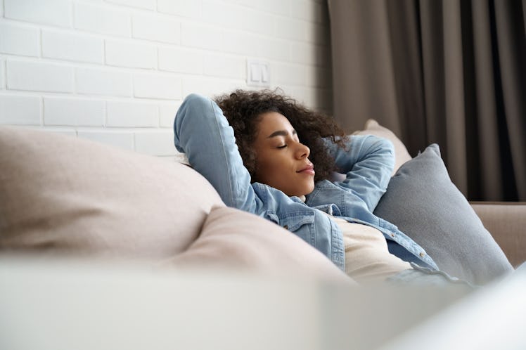 Relaxed tired young african american woman napping on comfortable sofa with eyes shut closed. Calm l...