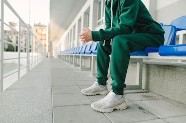 Cropped photo of a young man's legs in a green suit and bloodsuckers, sitting alone in the stands an...