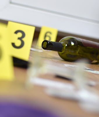 Broken glass and bottle of wine marked as evidence during crime scene investigation. Many yellow mar...