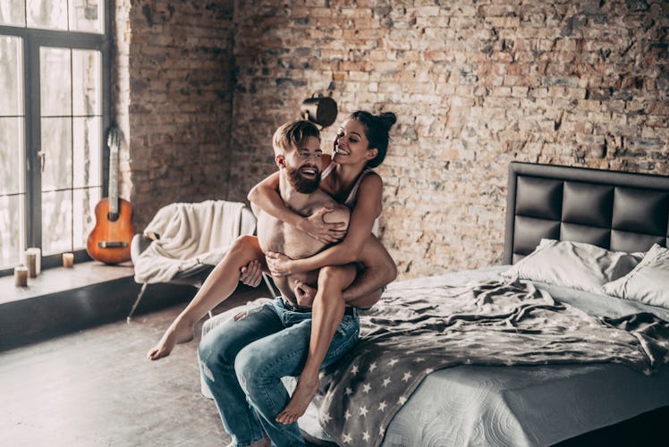 A couple playfully sits together on a bed.