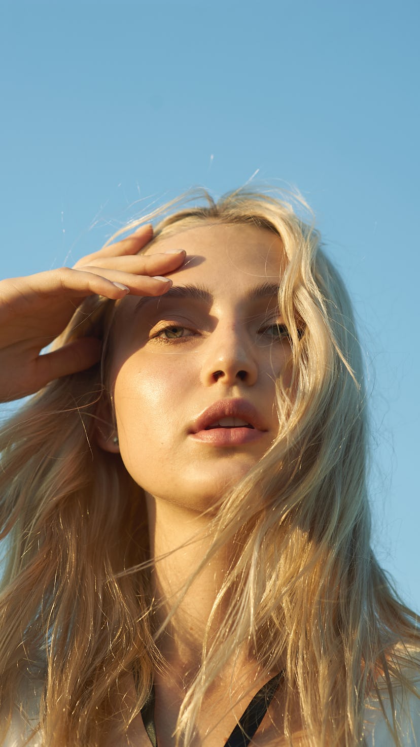 Gorgeous young woman in white romantic clothes on blue sky background. Sunny day. Blonde model with ...