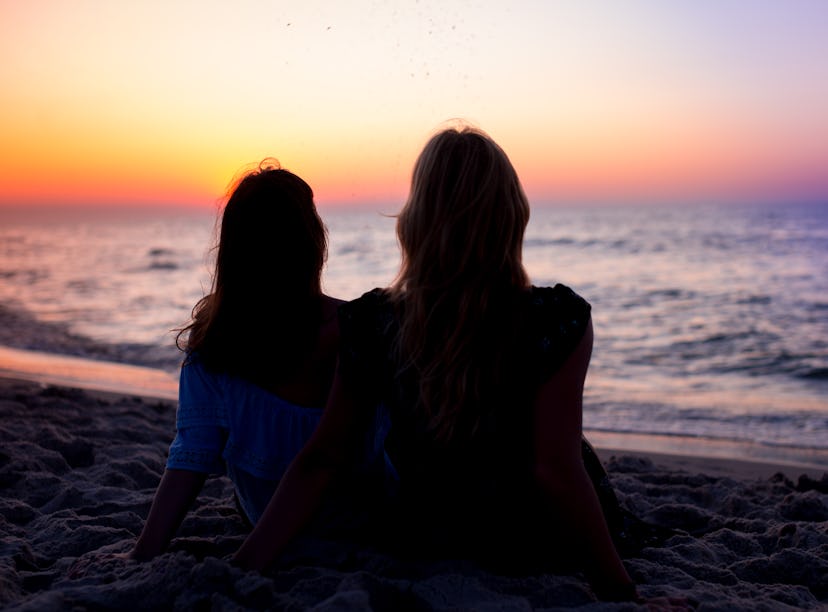 2 friends watching a sunset at the beach before posting a pic on Instagram with a pink sky caption.