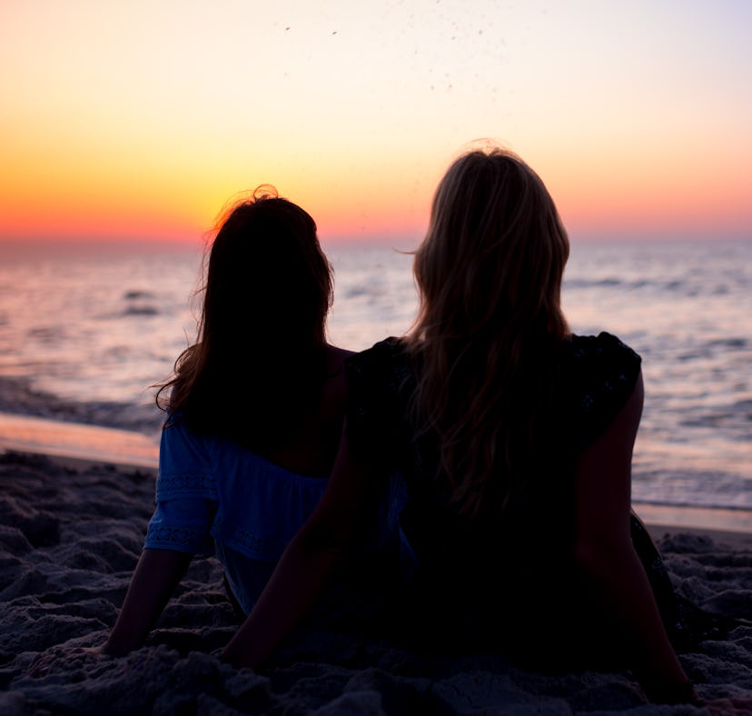 2 friends watching a sunset at the beach before posting a pic on Instagram with a pink sky caption.