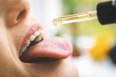 herbal alternative medicine and dietary supplements - woman taking cbd hemp oil drops in mouth from ...