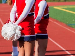 High school heeleaders holds thier poppoms behind their backs during football game.