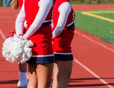 High school heeleaders holds thier poppoms behind their backs during football game.