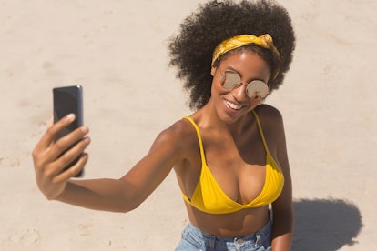 High angle view of young African American woman in yellow bikini and sunglasses taking selfie with h...