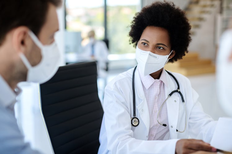 Black female doctor communicating with a patient while wearing protective face mask during medical a...