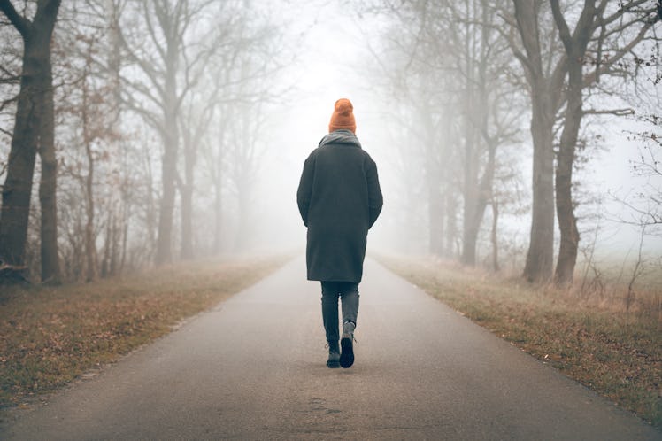 Back view of a woman walking into the distance on a foggy road