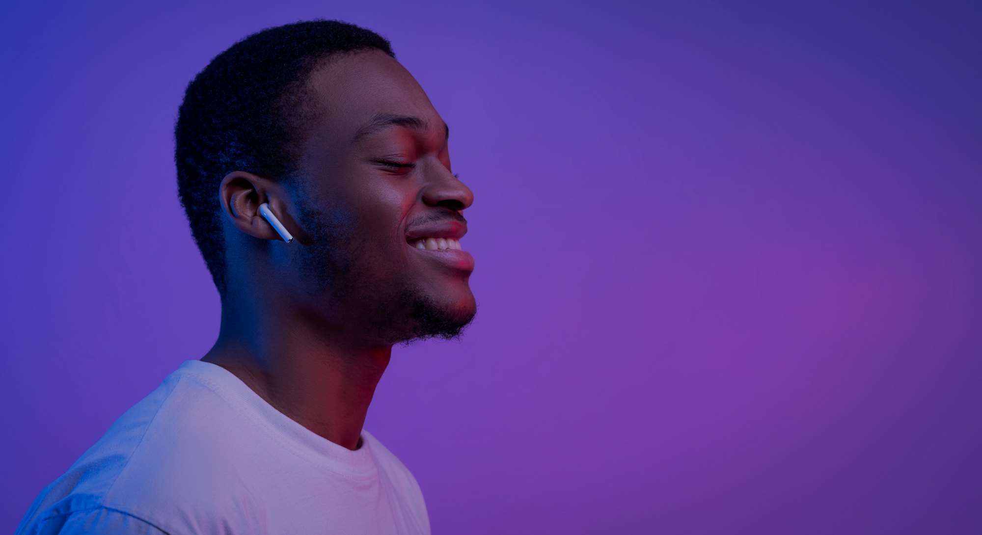 Relaxed African American Man Listening Music In Wireless Airpods Earphones In Neon Light, Smiling Bl...