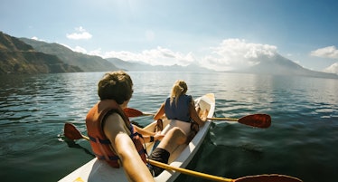 Outdoor Nature Selfie of Young Lovely Couple Canoeing Kayaking on Sunny Day on Lake Sea with Mountai...