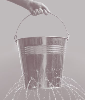 Woman holding leaky bucket with water on light grey background, closeup