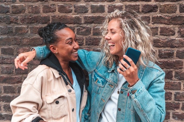 Happy lesbian couple embracing and laughing - Multiracial lesbian women, millennials, having fun tog...
