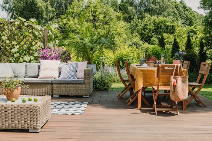 Dining table covered with orange tablecloth standing on wooden terrace in green garden
