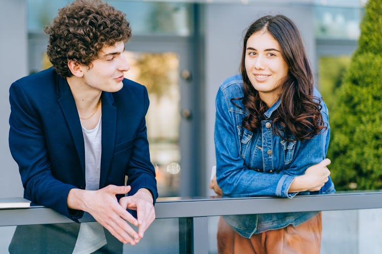 Young diverse students talking during break outdoor over university building, enjoying live communic...