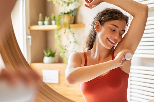 Beautiful young woman using deodorant under armpit in bathroom during morning time. Girl applying de...