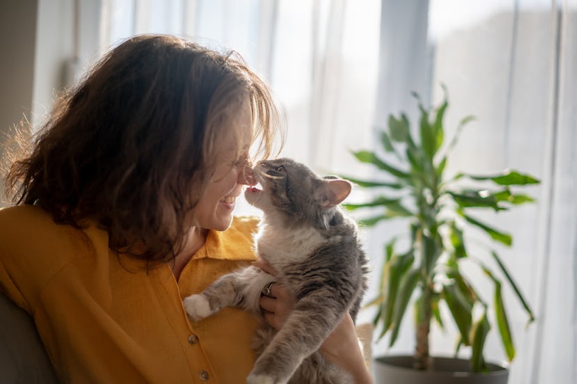 a woman snuggling with a cat, who bites her nose