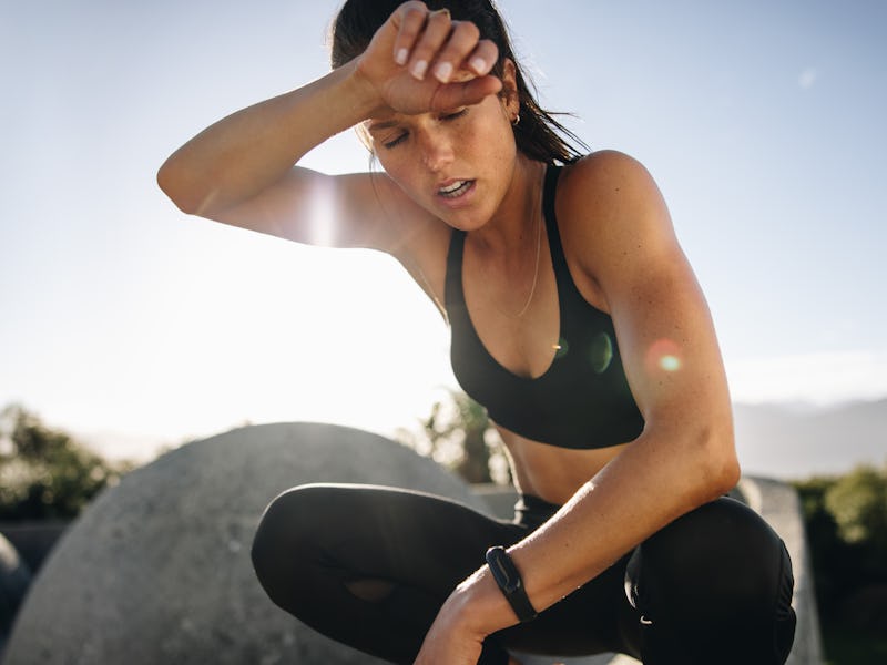 Tired woman sitting and resting after workout. Woman feeling exhausted after training session wiping...