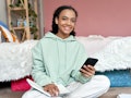 Happy african american teen girl high school student holding cell phone distance learning class usin...