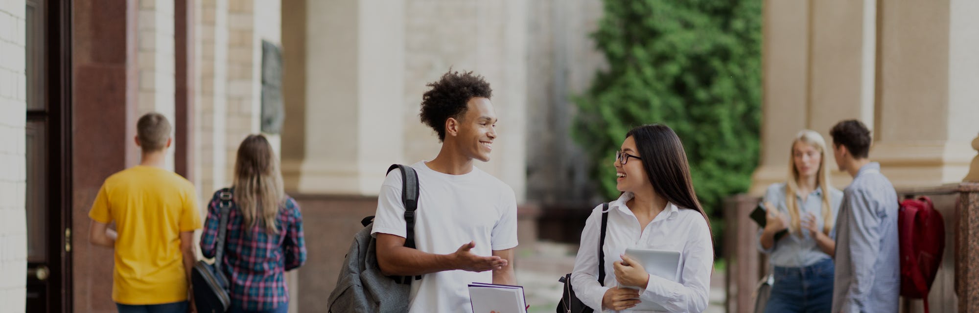 Diverse classmates chatting, walking after classes in university campus outdoors