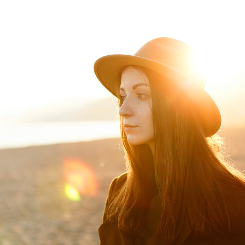 Sad young woman wearing a hat in the sunlight, feeling the summertime sadness throughout the month o...