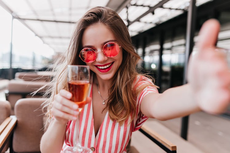 Young woman taking selfie while holding a glass of rosé to pair with rose captions for Instagram or ...