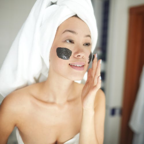 Portrait of beautiful Asian woman applying face mask during beauty treatment looking in mirror and s...