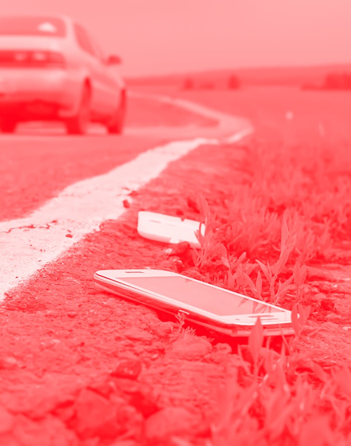 a discarded broken mobile phone is lying on the asphalt against the background of a passing car