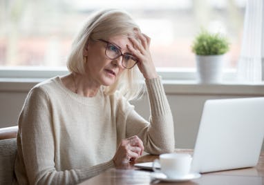 Thoughtful confused mature business woman concerned thinking about online problem looking at laptop,...