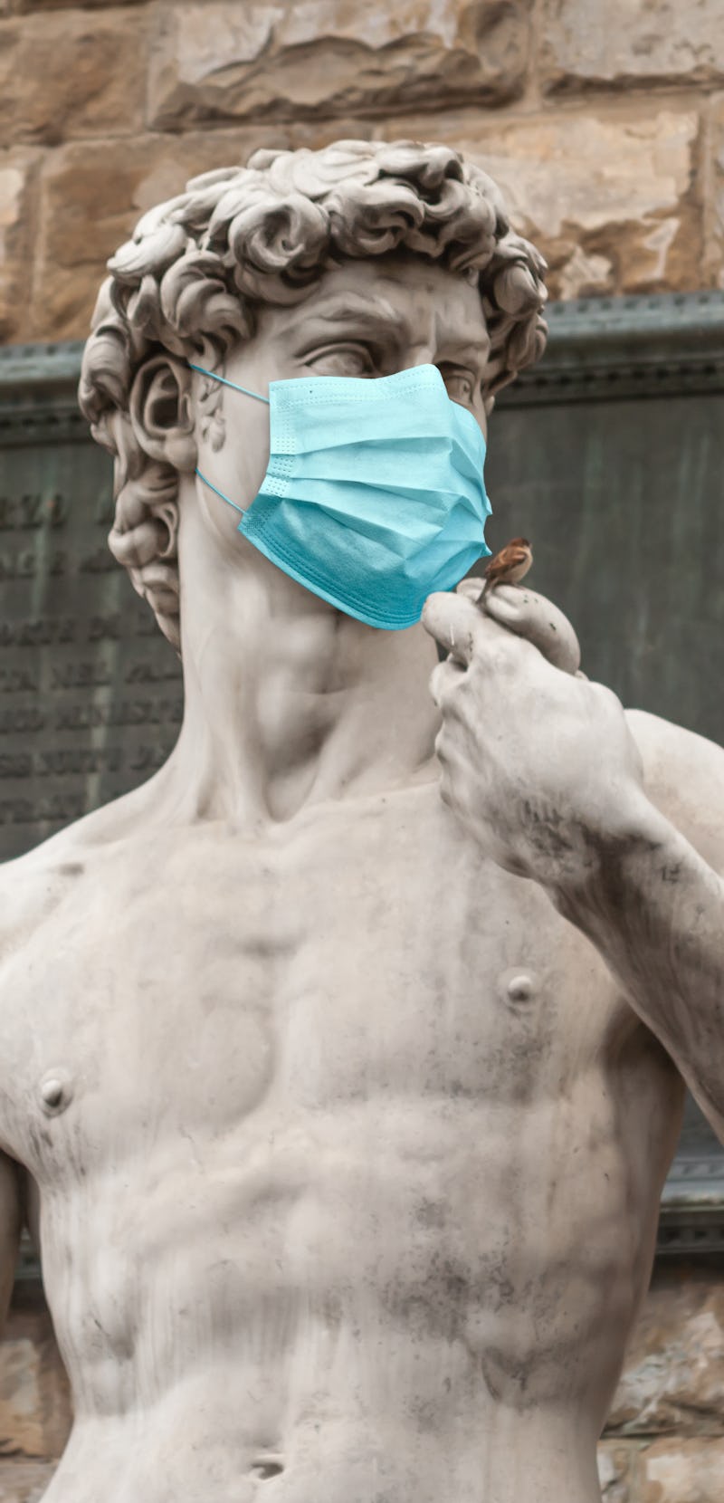 The Statue Of David in the Piazza della Signoria In Italy Wearing Blue Protective Medical Face Mask.