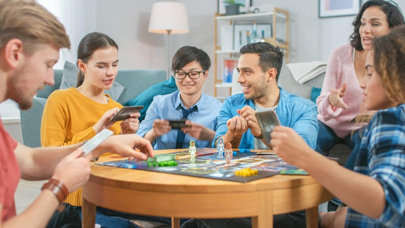 Diverse Group of Guys and Girls Playing in a Strategic Board Game with Cards and Dice. Cozy Living R...