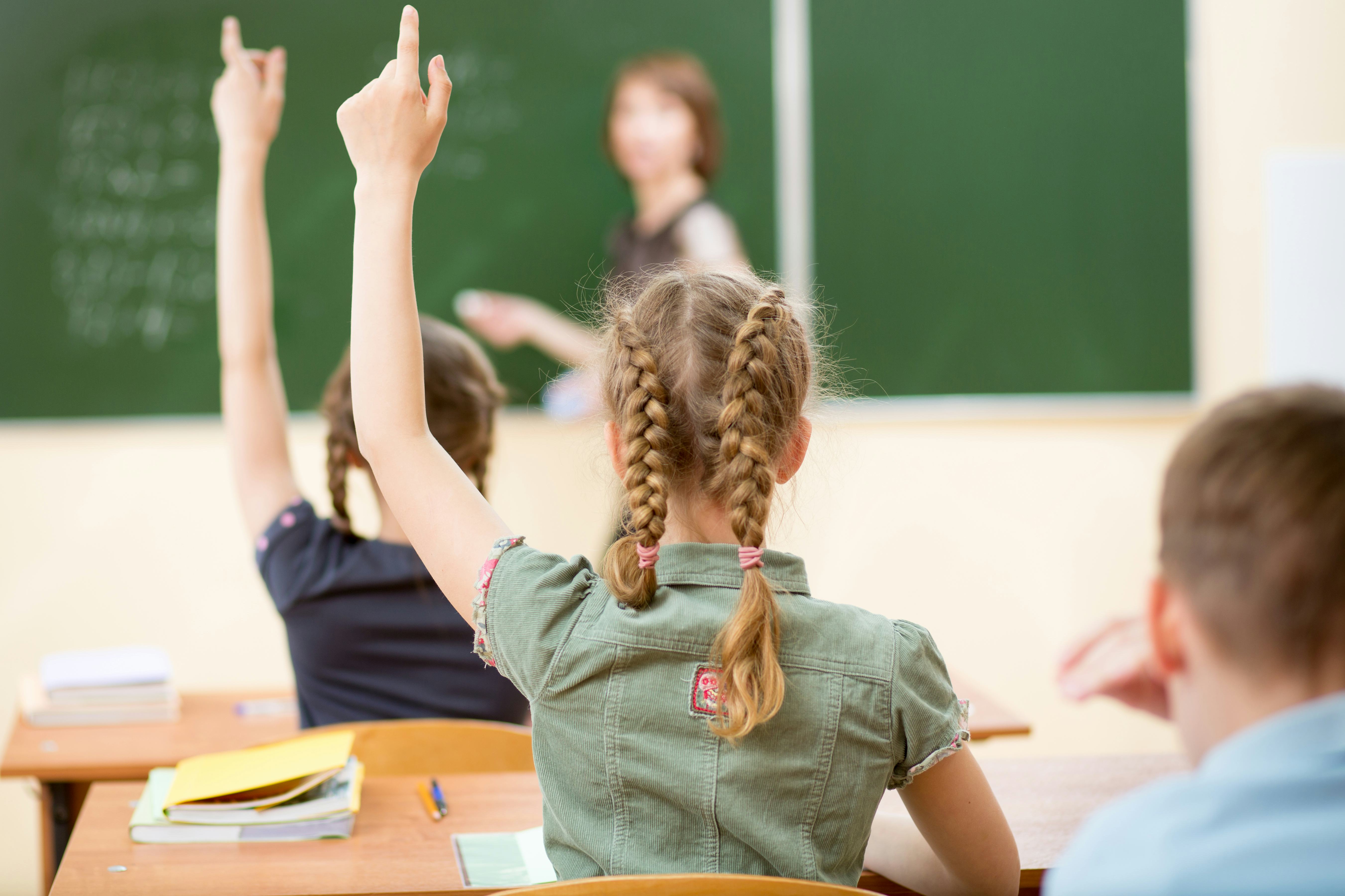 School children in classroom at lesson. Teacher standing at chalkboard.