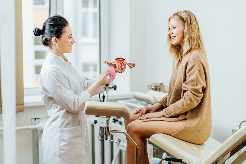 A gynecologist talking to her patient while holding a female reproductive organs model in her hand
