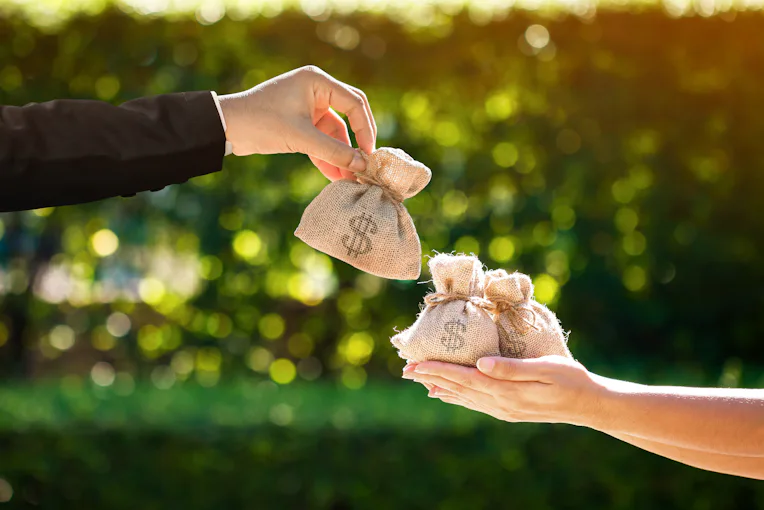Businessman and a woman hands hold a money bags in the public park for loans to planned investment i...