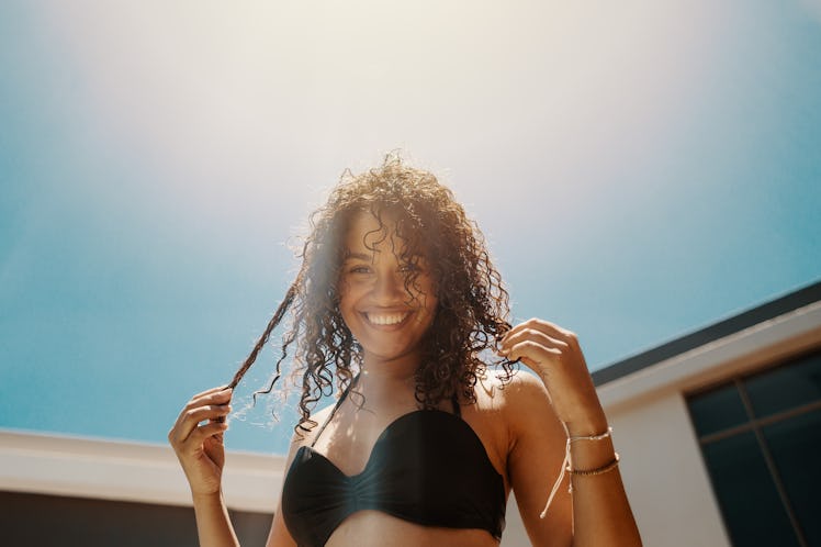 Young woman in swimsuit having great time by swimming pool outdoors