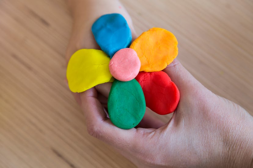 Image of hands holding a colorful flower made of clay, or Play-Doh. 